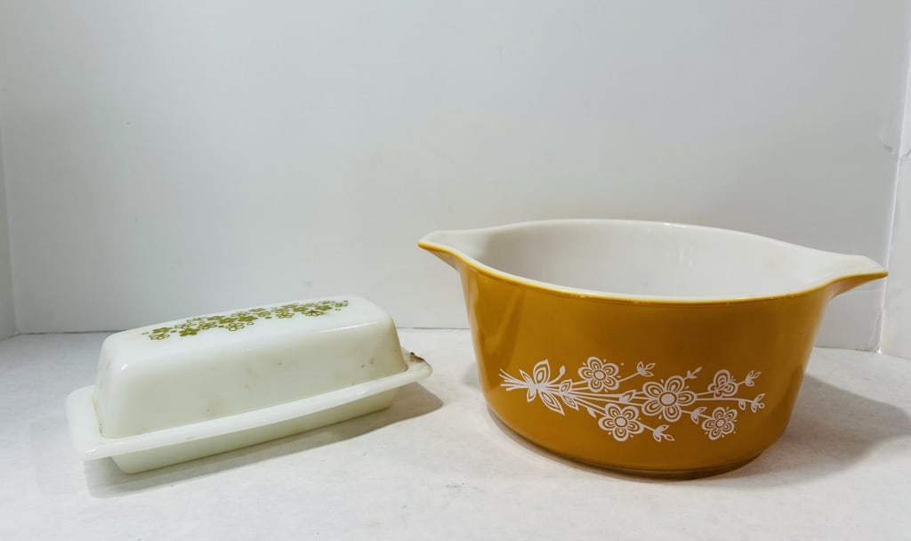 Two Pieces of Vintage Milk Glass Kitchenware in Patterns Attributed to Pyrex: This lot consists of two pieces of vintage opal milk glass kitchenware featuring mid-century floral motifs. Included is a rectangular lidded butter dish with a white base and matching lid decorated wi