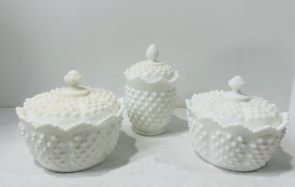 3 White Hobnail Milk Glass Lidded Vessels Attributed to Fenton: A trio of white milk glass lidded vessels featuring a hobnail pattern, attributed to the Fenton Art Glass Company. The collection includes two oval-form bowls, likely intended as sugar or candy dishes