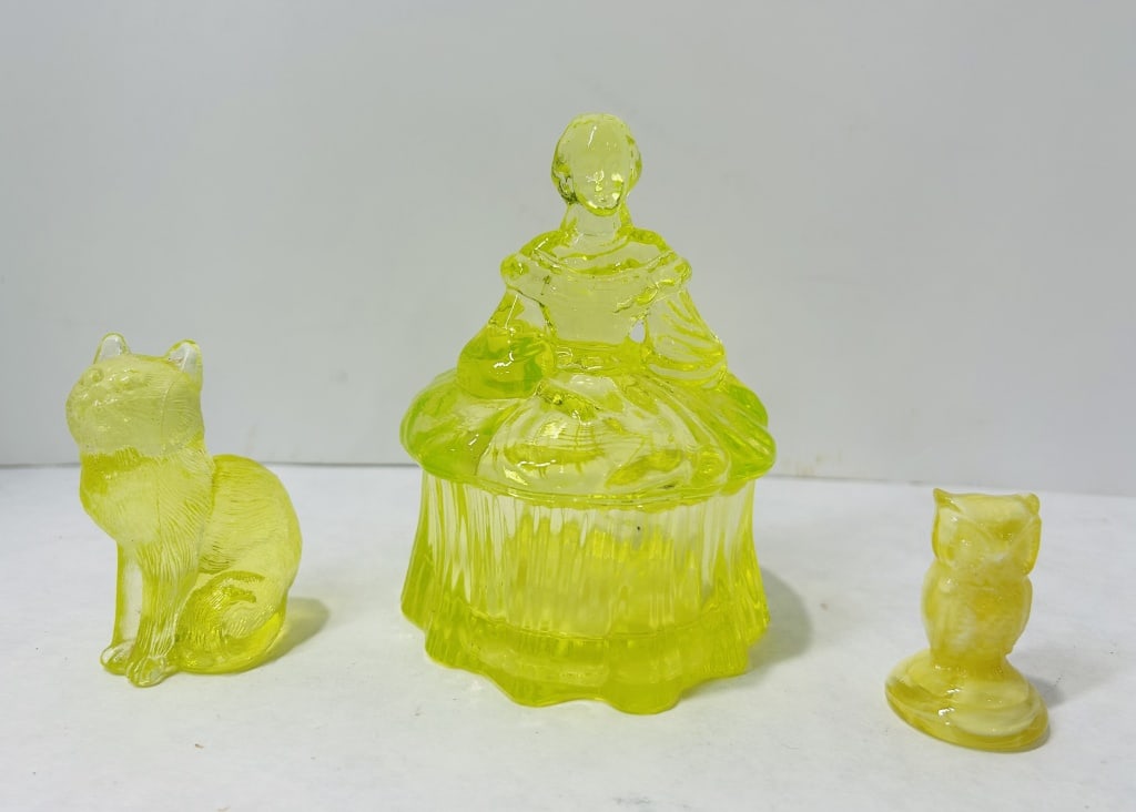 A Trio of Yellow Uranium Glass Decorative Items: A trio of yellow uranium glass objects comprising a seated cat figurine, a Southern Belle figural trinket box, and a small owl figurine. The cat and the trinket box are produced in translucent canary 