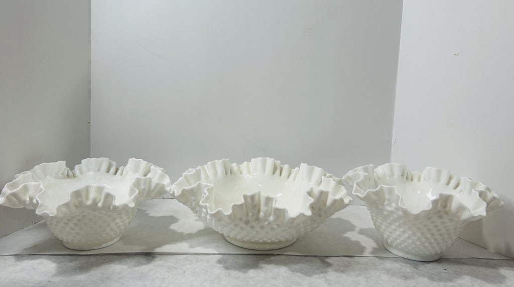 A Trio of Fenton White Hobnail Milk Glass Ruffled Bowls: A trio of white milk glass bowls manufactured by Fenton Art Glass. Each piece features a relief hobnail pattern on the exterior surface and a double-crimped, ruffled rim. The items vary in depth and c