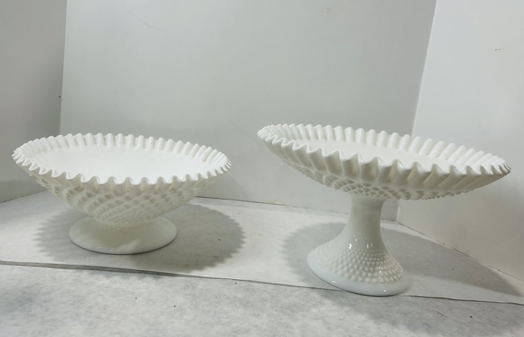 Two Pieces of White Hobnail Milk Glass Tableware Attributed to Fenton: A group of two opaque white milk glass serving pieces featuring a hobnail textured pattern. The lot consists of a large, low footed bowl and a pedestal cake stand. Both items are designed with charact