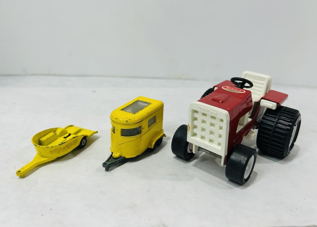 Vintage Tonka and Tonka Style Pressed Steel and Farm Toys: A trio of vintage toy farm vehicles including a red and white tractor and two yellow trailers. The tractor is constructed of pressed steel and plastic and features a white grille, a white seat, and a 