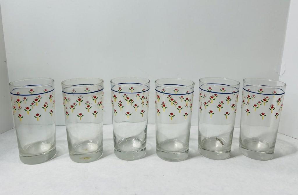 Mid-Century Modern Screen-Printed Floral Glass Tumblers: A group of clear glass tumblers featuring a cylindrical form with weighted bases. The exterior of each glass is decorated with a screen-printed pattern consisting of a single horizontal blue band belo