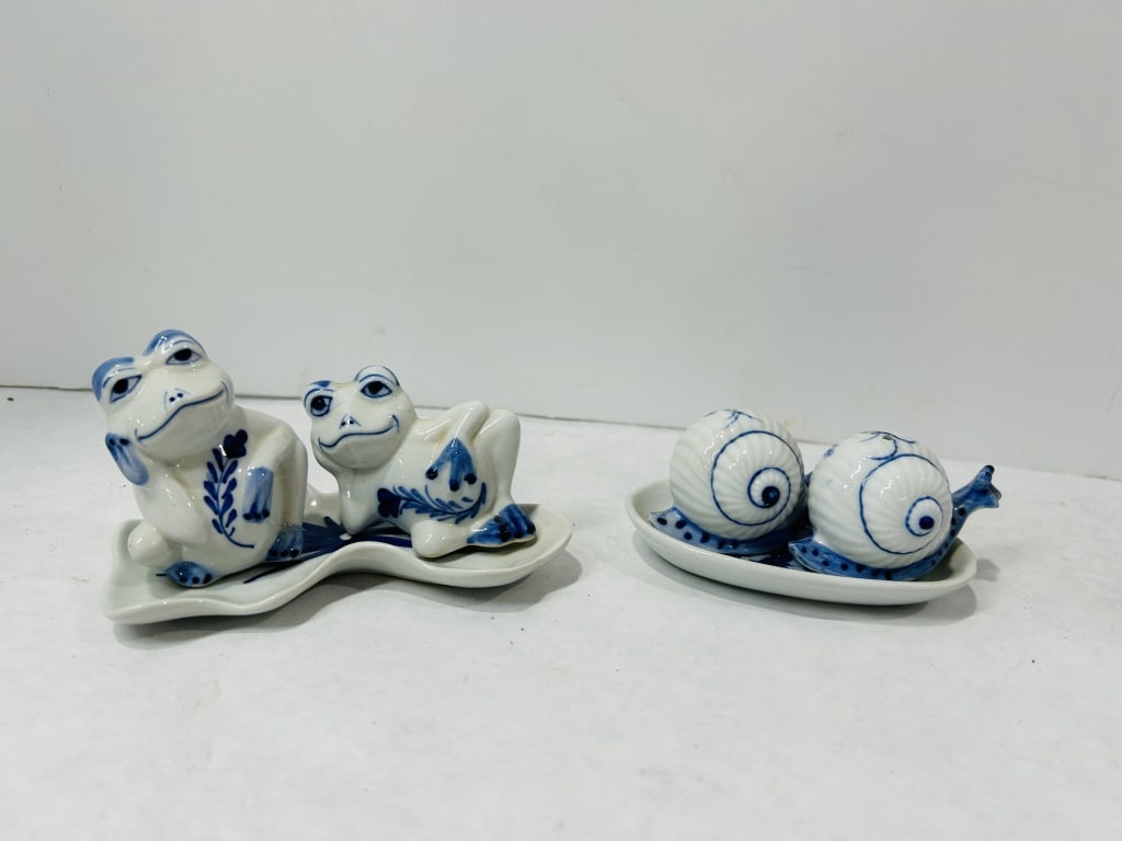 Blue and White Ceramic Salt and Pepper Shakers: A collection of blue and white glazed ceramic salt and pepper shakers with matching underplates. The group includes frog figurines in varied poses, including one seated and one reclining, decorated wi