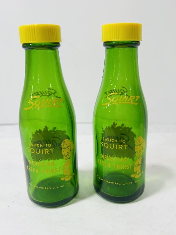 A Pair of Vintage Squirt Green Glass Miniature Bottles: A pair of miniature green glass bottles featuring red and yellow applied color labels (ACL) for the Squirt soda brand. The obverse of each bottle displays the brand name in red lettering over a yellow