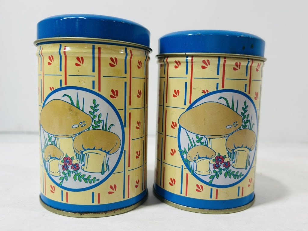 A Pair of Vintage Lithographed Tin Kitchen Shakers in the Style of Sears Merry Mushroom: A pair of vintage lithographed tin kitchen shakers featuring a decorative motif in the style of the Sears Merry Mushroom pattern. Each cylindrical vessel is constructed from sheet metal with a cream-c