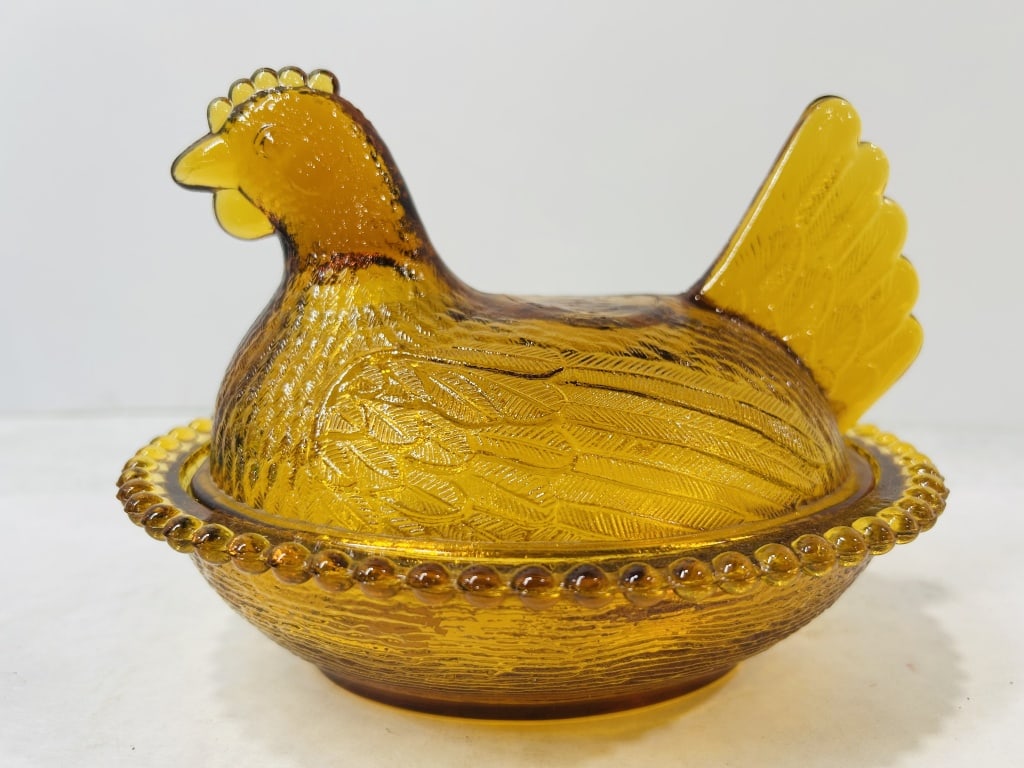 Amber Indiana Hen on Nest Covered Dish: A pressed glass covered candy dish executed in a translucent amber-colored glass. The piece is modeled in the form of a hen on a nest, consisting of a figural lid and a separate base. The lid features