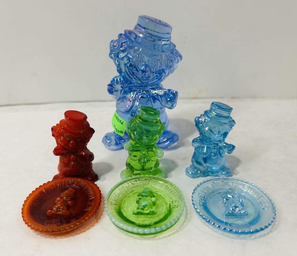 Mosser The Musical Fiddler Figurines and Plates: A collection of pressed glass decorative items featuring a character identified as The Musical Fiddler. The group includes several figurines of varying sizes and matching miniature plates in