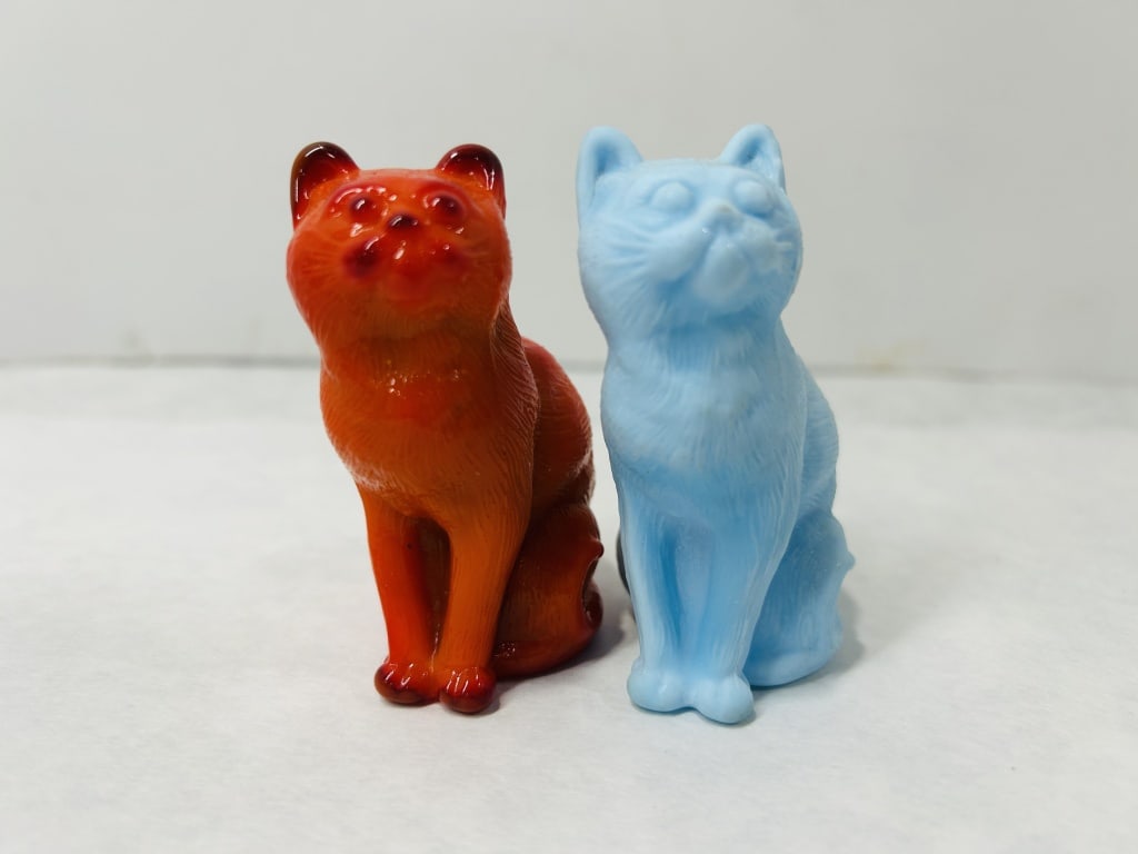 Mosser Glass Sitting Cat Figurines: A pair of small pressed glass figurines in the form of seated cats, attributed to Mosser Glass. Each figurine is rendered in a matching pose with its head tilted upward and features molded details rep