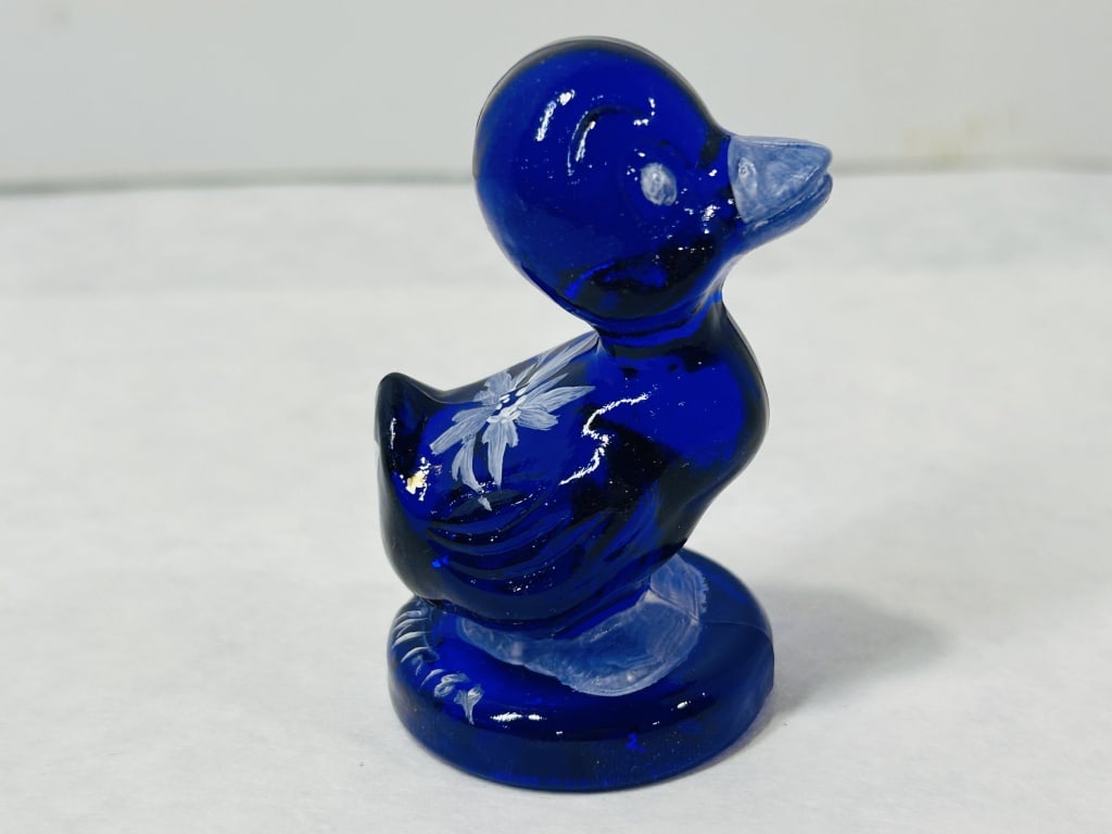 Boyd Crystal Art Glass Cobalt Blue Debbie Duck Figurine: A cobalt blue pressed glass duckling figurine in the Debbie Duck pattern, produced by Boyd Crystal Art Glass. The duck is modeled in a seated position on an integrated circular base. The translucent g