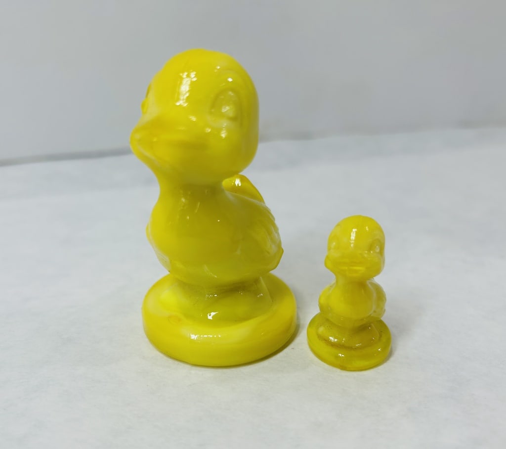 Boyd Yellow Slag Glass Duck Figurines: A pair of opaque glass figurines depicting an adult duck and a matching duckling. Both pieces are crafted from vibrant canary-yellow slag glass featuring subtle white marbling throughout the material.