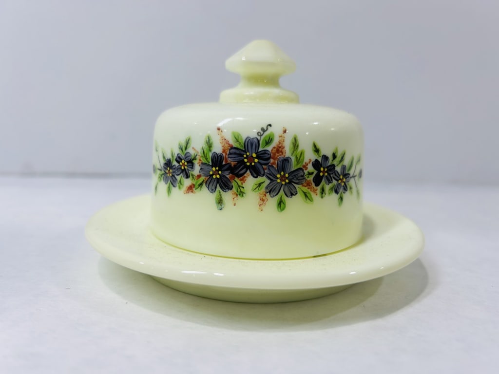 Fenton Custard Uranium Glass Lidded Butter Dish: This two-piece set features a circular underplate and a matching domed cover, both crafted from opaque custard-colored glass. The material fluoresces bright green under ultraviolet light, confirming t
