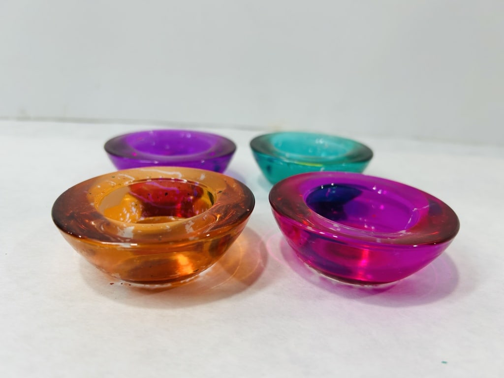 Colorful Glass Tea Light Candle Holders: A group of translucent glass tea light candle holders attributed to Crate and Barrel. Each circular holder is constructed of thick molded glass in vibrant shades of teal green, deep purple, orange-amb