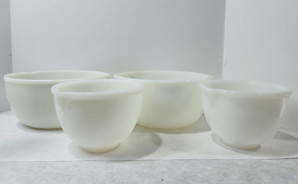 Vintage White Milk Glass Nesting Mixing Bowls in the Style of Glasbake: This group of nesting mixing bowls is crafted from opaque white milk glass. Each piece features a rounded body with a flared rim and two integrated pouring spouts or lugs situated on opposing sides. T