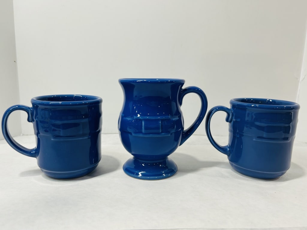 Longaberger Blue Glazed Ceramic Mugs and Footed Vessel: A trio of cobalt blue glazed ceramic drinkware pieces, comprising two matching mugs and one footed pedestal vessel. Each piece is constructed with a molded relief design featuring geometric rectangula