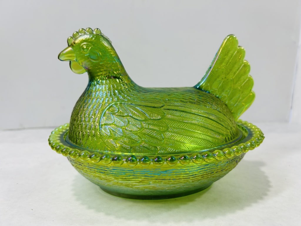 Green Iridescent Carnival Glass Hen on Nest: This two-piece pressed glass covered dish features a nesting hen figure and is attributed to the Indiana Glass Company. The piece is composed of green glass finished with a strong iridescent carnival 