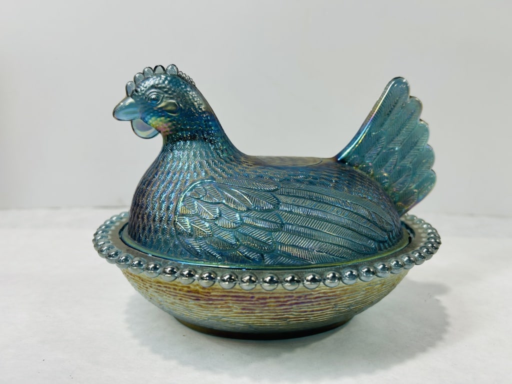 Iridescent Blue Carnival Glass Hen on Nest Dish: This two-piece lidded dish is crafted in iridescent blue carnival glass, showing characteristics attributed to the Indiana Glass Company. The set includes a lid molded in the form of a seated hen with