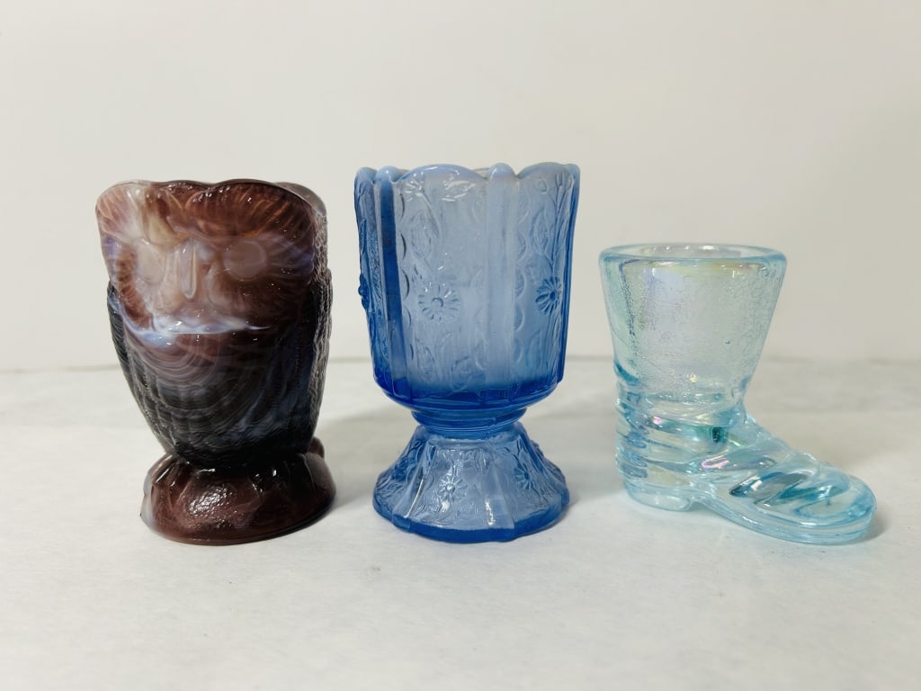 A Trio of Vintage Novelty Glass Toothpick Holders: A trio of vintage pressed glass novelty toothpick holders featuring different forms and techniques. The collection includes one holder modeled as an owl in purple and white swirled slag glass, a style