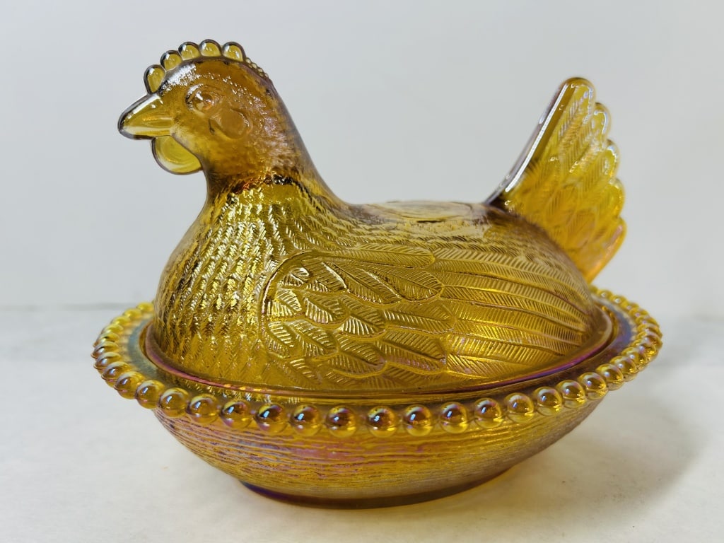 Marigold Carnival Glass Hen on a Nest Candy Dish, Indiana Glass Company: This two-piece pressed glass covered dish, commonly referred to as a Hen on a Nest, features a marigold iridescent finish over an amber glass body, characteristic of carnival glass. The lid is modeled