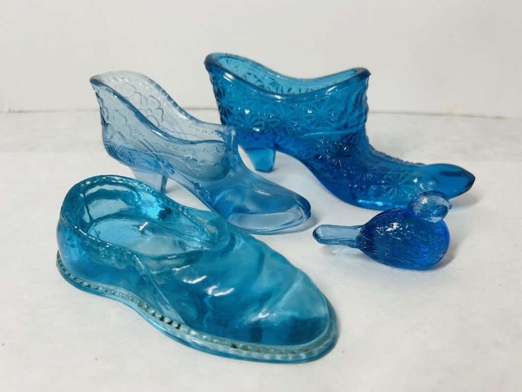 An Assortment of Vintage Blue Pressed and Art Glass Decorative Items Including Fenton: This collection features various decorative glass items in shades of aqua, teal, and cobalt blue. A light blue pressed glass slipper is decorated with a raised floral and scroll pattern and bears a mo