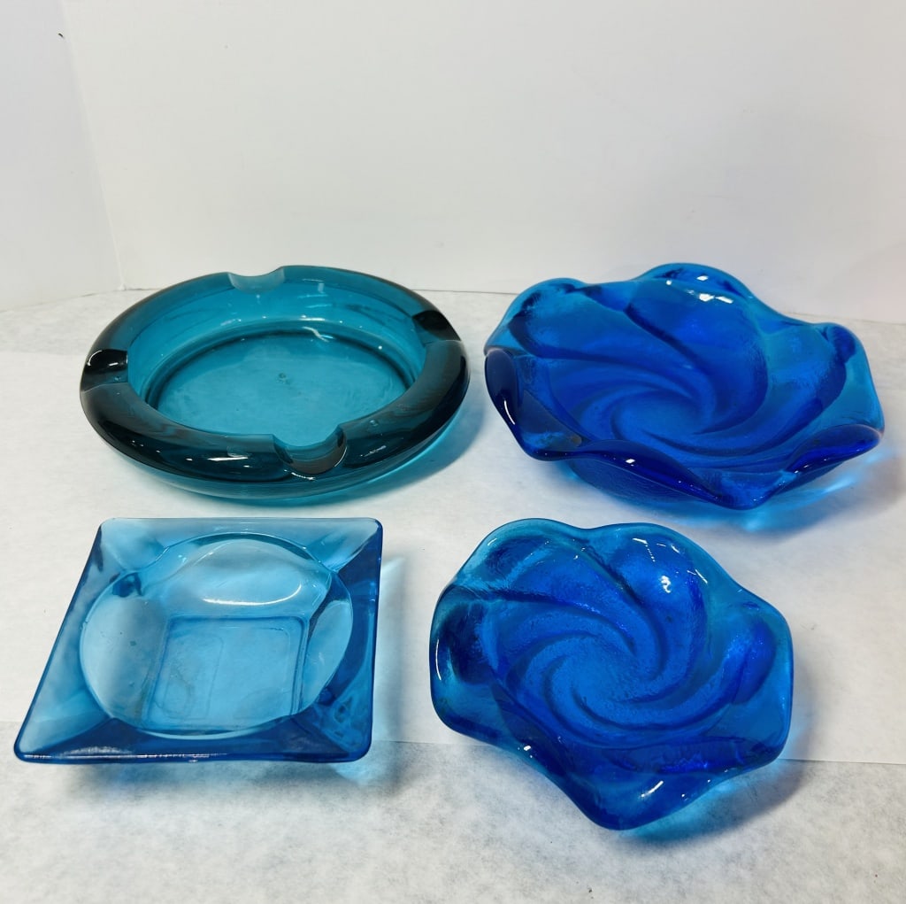 A Collection of Mid-Century Modern Blue Art Glass Ashtrays and Decorative Dishes: This collection features several pieces of mid-century modern style molded glass in a variety of blue tones. Included is a large, heavy circular art glass ashtray in a deep teal or aquamarine color, d