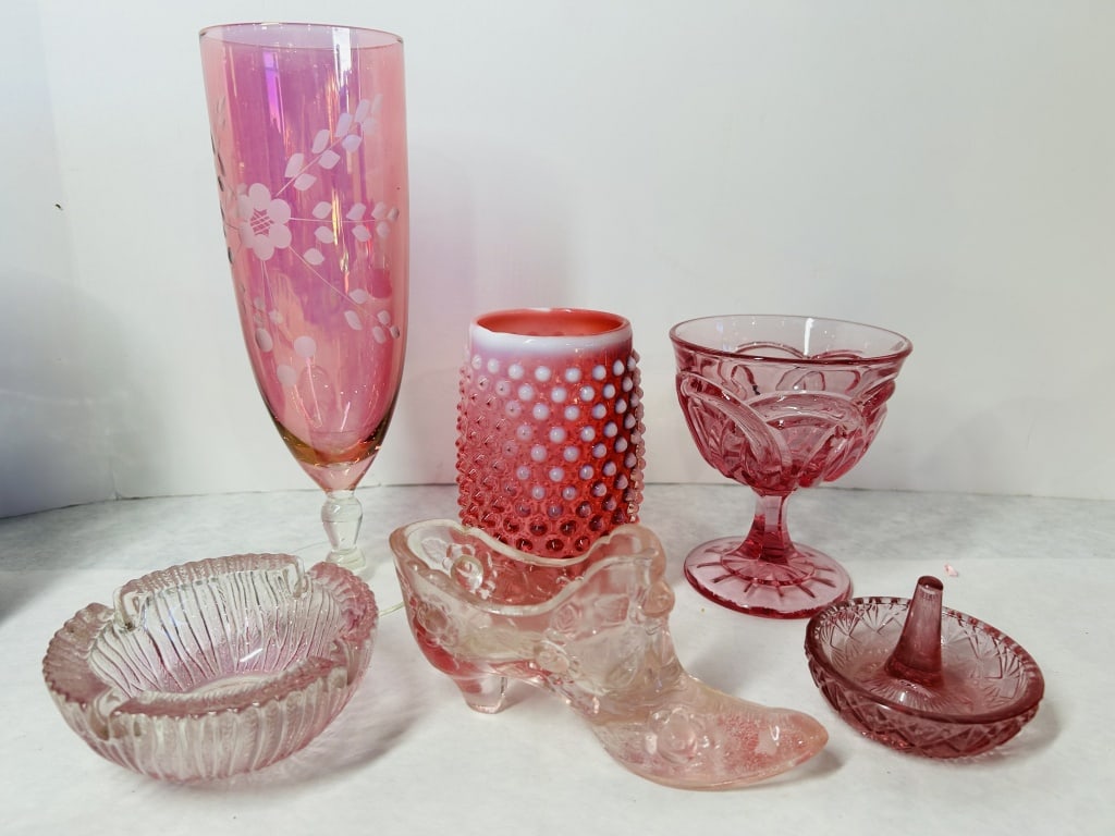 An Assortment of Six Pieces of Vintage Pink and Red Decorative Glassware: This six-piece collection of vintage decorative glassware consists of various pink and red vessels and objects produced in the mid-20th century. The set includes a tall pink iridescent pilsner glass f