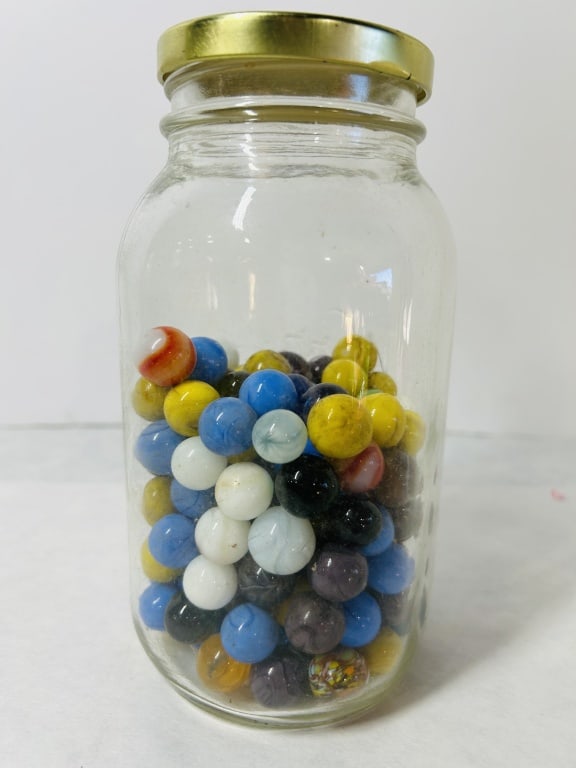 A Collection of Assorted Glass Marbles in a Kerr Self Sealing Mason Jar: A collection of assorted glass marbles contained within a clear glass jar. The jar is embossed on the side with the brand name Kerr in cursive script above the block lettering SELF SEALING MASON. The 