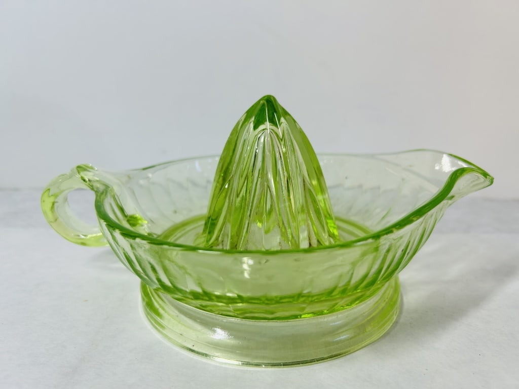 Vintage Uranium Green Depression Glass Citrus Juicer Reamer: This vintage citrus reamer is crafted from translucent pale green glass, commonly known as uranium glass. The piece consists of a central conical reamer integrated into a shallow bowl featuring a sing