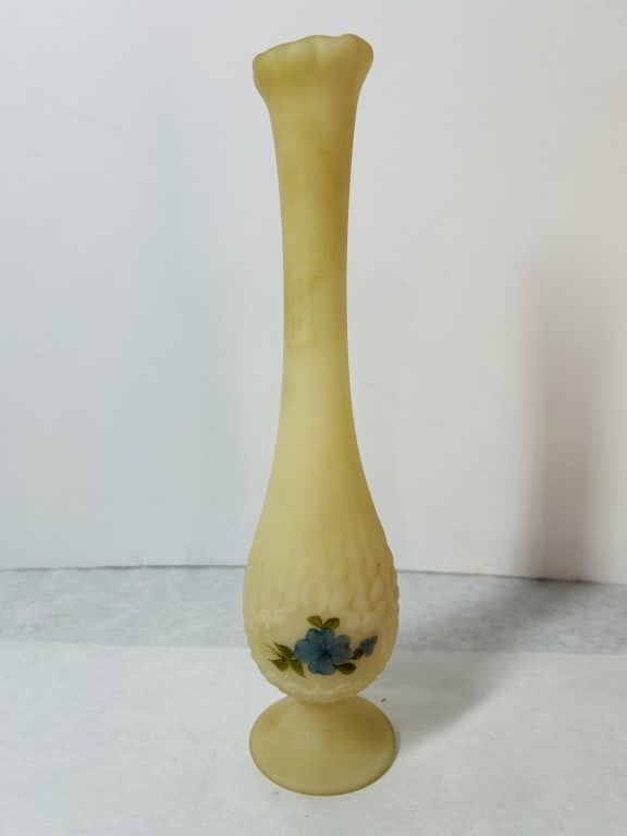 Fenton Hand Painted Custard Glass Bud Vase: A tall custard glass bud vase with a pale yellow satin finish, produced by Fenton. The vessel features a bulbous base decorated with a molded relief pattern and a slender, elongated neck terminating i