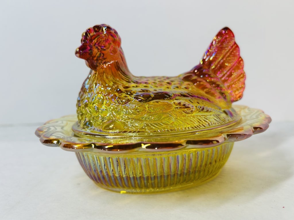Marigold Iridescent Amberina Mosser Glass Hen on Nest Covered Dish: This two-piece covered glass dish, featuring a hen on a nest design, is attributed to the Indiana Glass Company. The object is composed of amberina glass, which displays a color gradient from a yellow