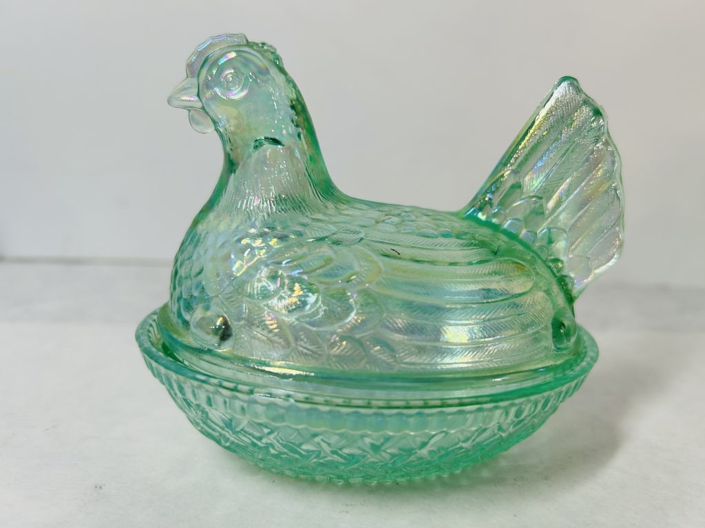 Iridescent Green Carnival Glass Hen on Nest Covered Dish: A two-piece covered pressed glass dish in the classic hen on nest form. The piece is crafted from translucent green glass with a multi-colored iridescent surface finish, often referred to as carnival 