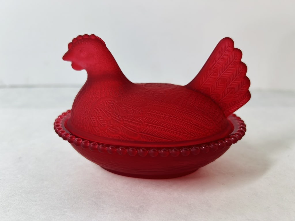 Red Satin Glass Hen on Nest Covered Dish: A vintage two-piece covered dish in the traditional hen on nest form. The object is composed of ruby red glass with a frosted satin finish applied to the exterior. The lid is molded in the shape of a 