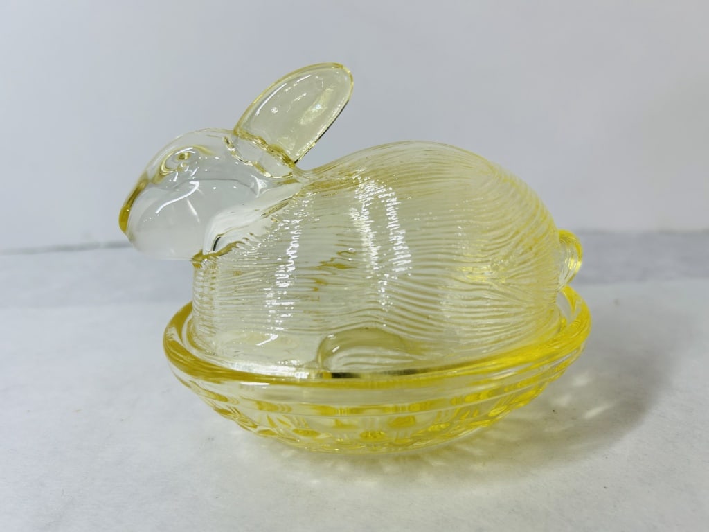 Yellow Pressed Glass Bunny on Nest Covered Dish: A two-piece covered dish or trinket box fashioned from transparent yellow pressed glass. The lid is molded in the form of a seated rabbit, featuring horizontal linear ribbing on the body to simulate f