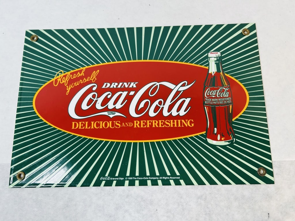 1999 Coca-Cola Porcelain Enamel Advertising Sign: This is an authorized reproduction Coca-Cola advertising sign produced in 1999. The rectangular sign is made of porcelain enamel on metal. The design features a green sunburst background with a centra