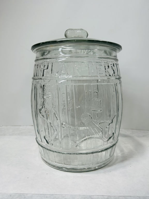 Vintage Planters Peanuts Barrel Shaped Glass Counter Jar with Lid: A large clear molded glass display jar designed in a barrel motif with embossed vertical staves and horizontal banding. The shoulder of the jar is embossed with the word PLANTERS in capitalized block 