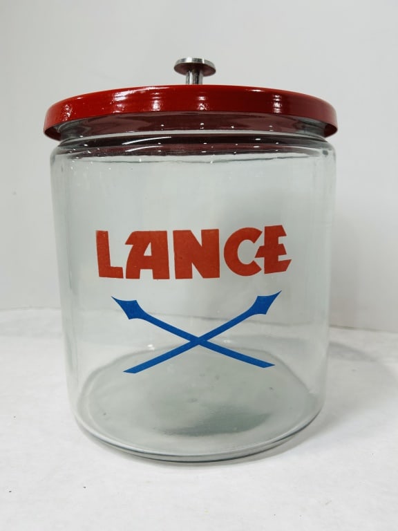 Vintage Lance Glass Counter Display Jar with Red Metal Lid: This vintage advertising counter display jar was produced for Lance snack foods, a prominent American snack company. The item is composed of a clear cylindrical glass jar with a red-enameled metal lid