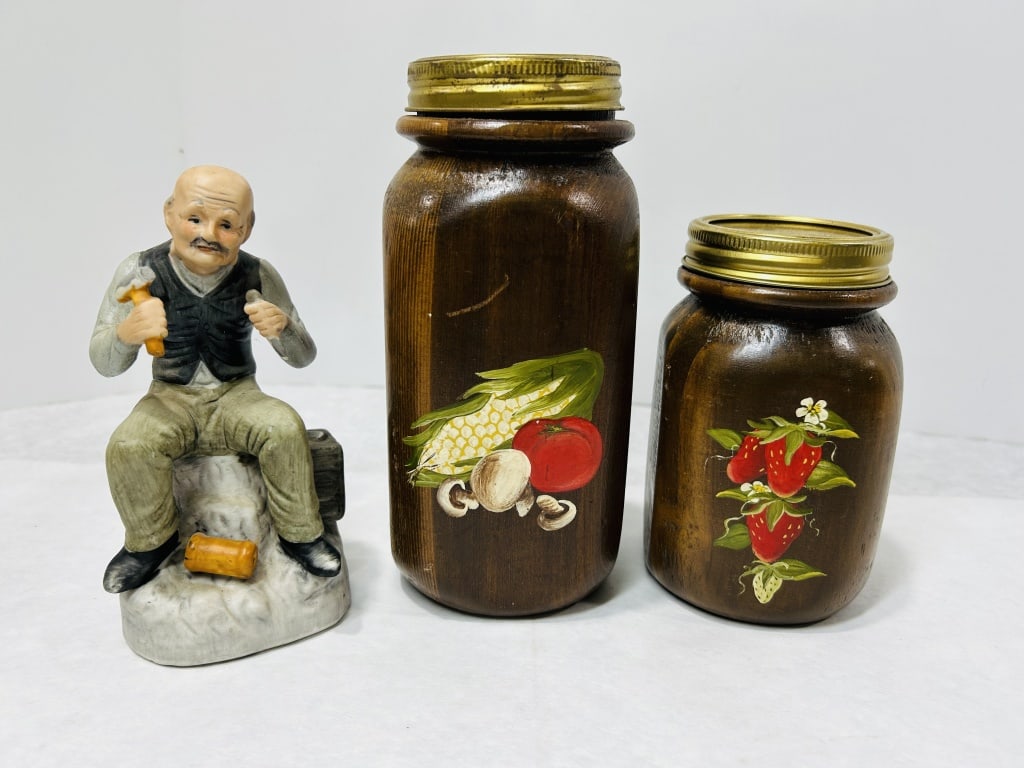 A Trio of Decorative Items Comprising a Ceramic Figurine and Two Hand-Painted Wooden Canisters: A trio of decorative objects including one painted ceramic figurine and two hand-painted wooden kitchen canisters. The ceramic figurine depicts an elderly male figure, portrayed as a craftsman or wood