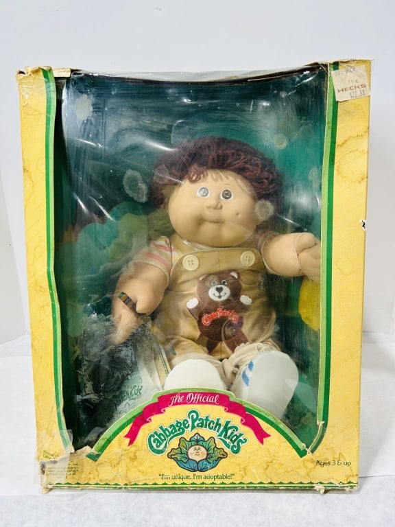 Coleco Cabbage Patch Kids Doll in Original Box: This vintage Cabbage Patch Kids doll was manufactured by Coleco. The doll features a vinyl head with brown eyes and dark brown curly yarn hair. It has a soft cloth body and is dressed in its original 