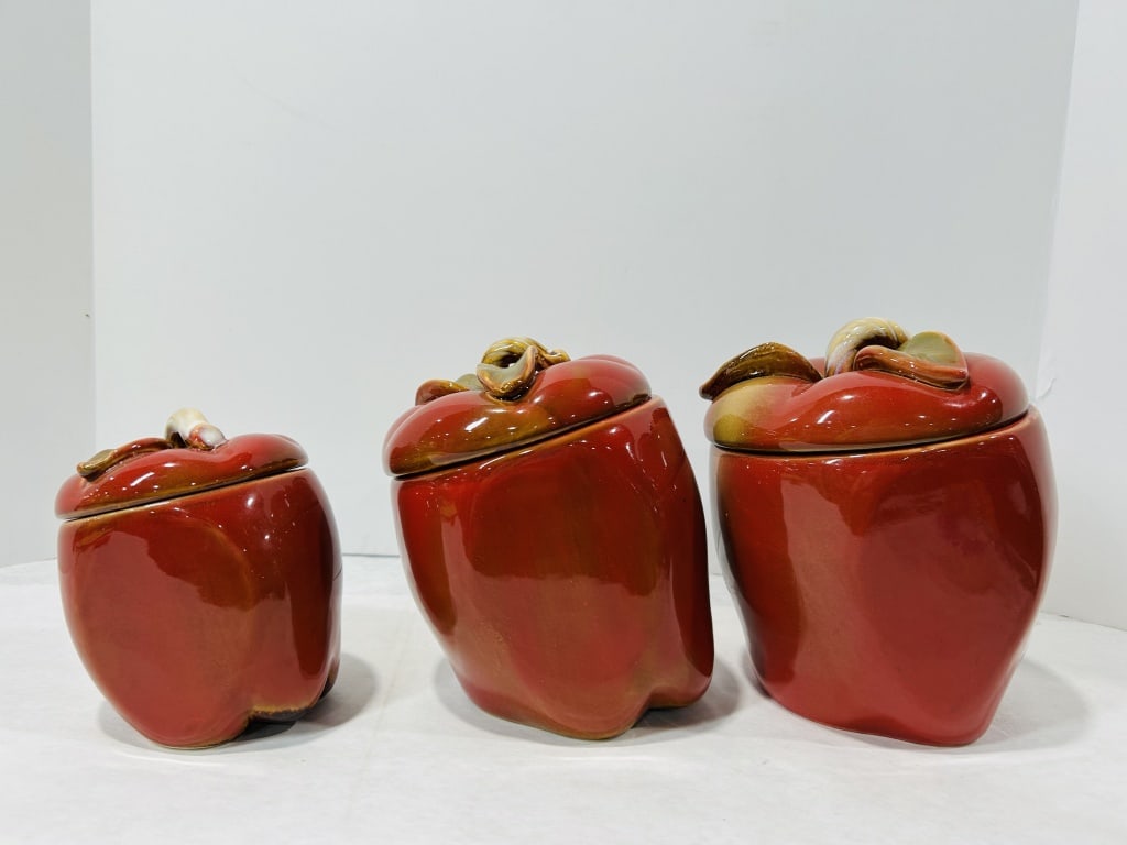 A Trio of Graduated Ceramic Apple-Shaped Canisters: This lot consists of a trio of graduated kitchen canisters crafted from ceramic and designed in the form of stylized apples. Each piece features a globular body with an indented base, finished in a hi