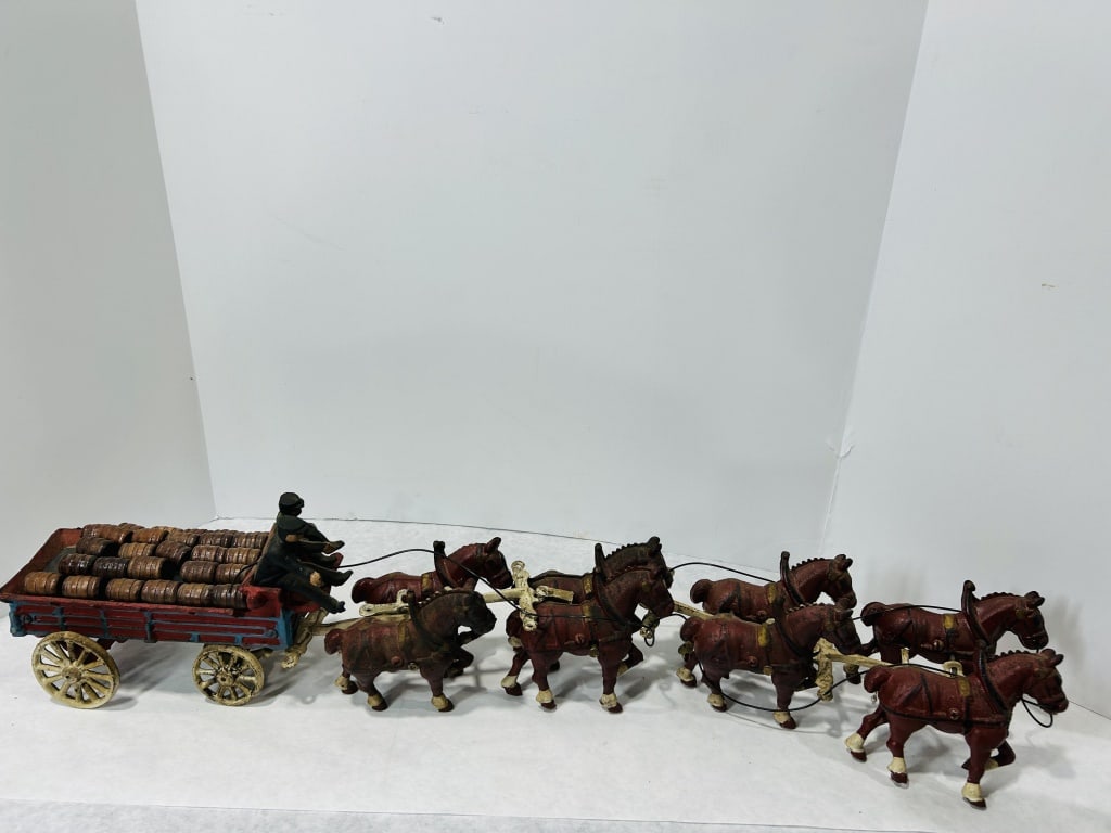 Antique Budweiser Eight-Horse Hitch Brewery Wagon: This antique cast iron toy is a Budweiser brewery wagon pulled by a team of eight horses. The wagon features a red-painted body with blue trim and cream-colored spoked wheels, carrying a full load of 