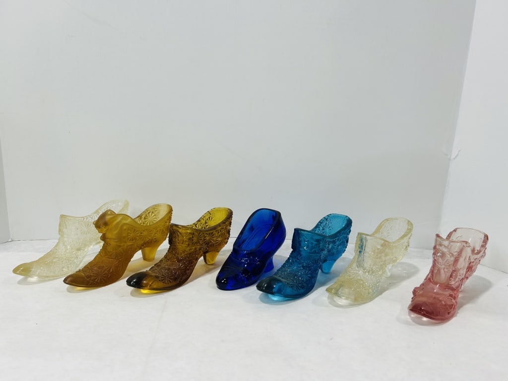 A Collection of Vintage Pressed Glass Slipper and Shoe Figurines: A collection of pressed glass shoe and slipper figurines in various colors and styles. The assortment includes high-heeled slippers, Victorian-style boots, and novelty kitten in a shoe figurines. Seve