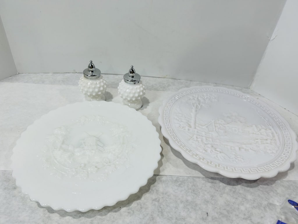 A Collection of Vintage White Milk Glass Including Scenographic Plates and Hobnail Salt and Pepper: A collection of vintage opaque white milk glass items featuring relief decoration. This group includes decorative plates with scalloped edges and salt and pepper shakers. One plate displays a central 