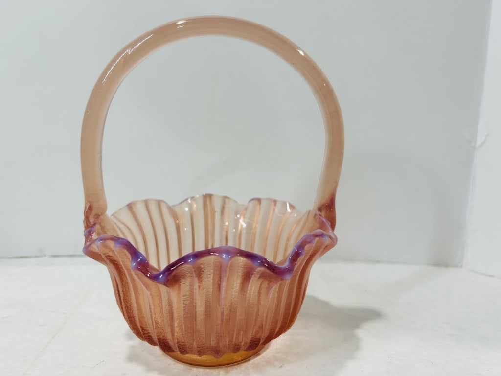 Pink Opalescent Ribbed Art Glass Basket with Blue Ruffled Rim: This art glass basket is attributed to Fenton Art Glass, consistent with mid-20th-century American decorative glass production. The piece features a vertically ribbed body made from peach or salmon-pi