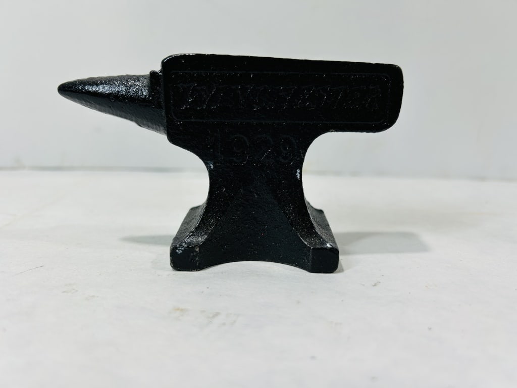 Winchester 1920 Miniature Cast Iron Promotional Anvil: This item is a miniature cast iron anvil bearing the branding of the Winchester Repeating Arms Company. The piece is modeled after a standard blacksmith anvil, featuring a tapered horn and a flat top 