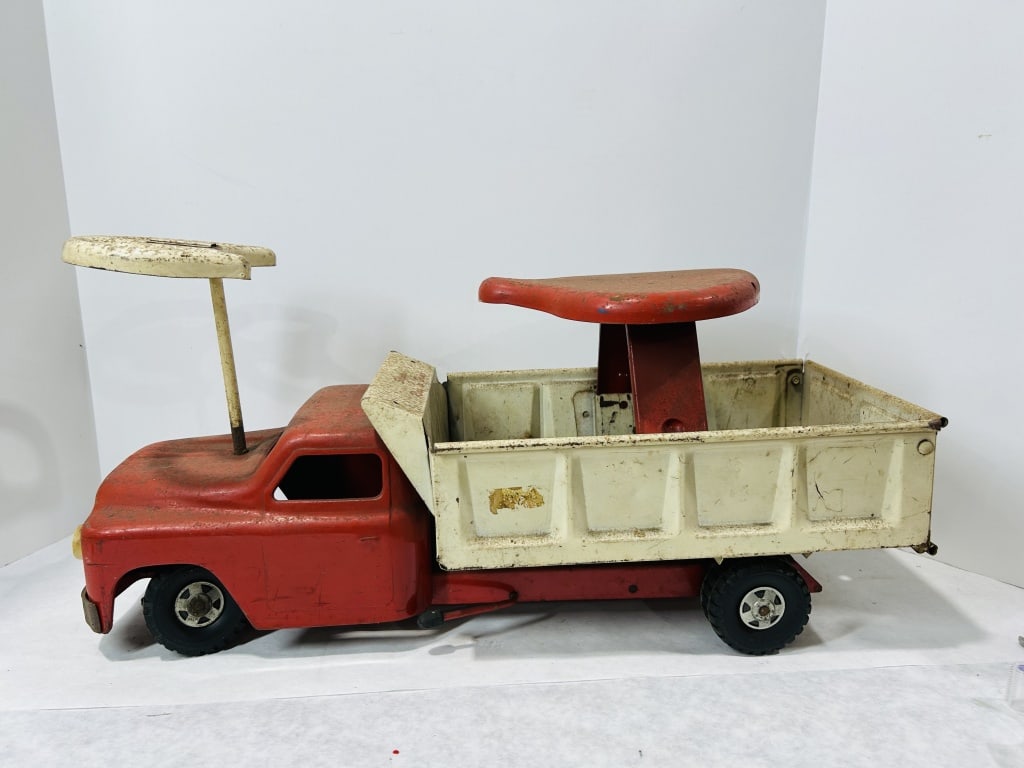 Structo Ride 'em Dump Ride-On Toy Truck: This is a large-scale vintage ride-on toy dump truck manufactured by the Structo Manufacturing Co. of Freeport, Illinois. The toy is constructed of pressed steel, featuring a red cab and chassis with 