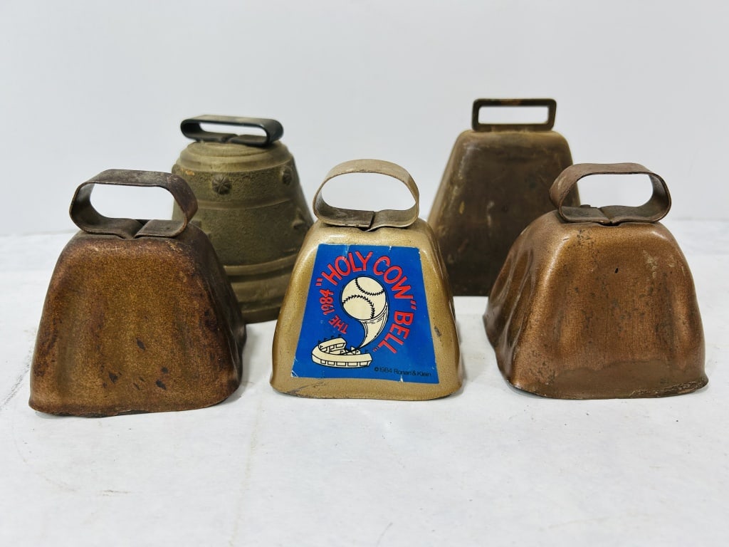 Collection of Five Vintage Cowbells including 1984 Chicago Cubs Holy Cow Commemorative Bell: This collection consists of five vintage metal cowbells of various styles and finishes. The central item is a gold-tone commemorative bell featuring a large blue, white, and red sticker on the front f