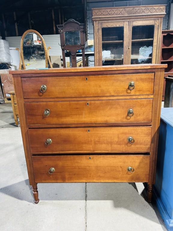 American Sheraton Style Four-Drawer Cherry Chest, Mid-19th Century: An American four-drawer chest of drawers in the Sheraton style, dating to the mid-19th century. The piece is constructed primarily from cherry wood with a warm finish. It features a rectangular overha