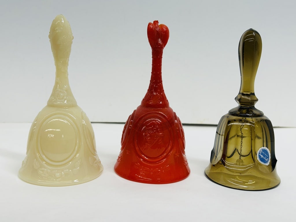 FENTON AND IMPERIAL GLASS BELLS, 1970S: A trio of American art glass hand bells comprising a Fenton Bicentennial red slag bell, an Imperial thumbprint bell, and a floral custard glass bell. A script Fenton mark and Imperial manufacturer sti