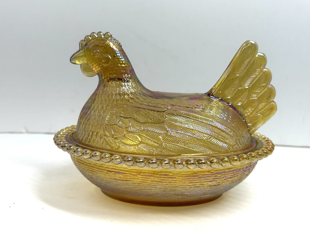 MARIGOLD IRIDESCENT GLASS HEN ON NEST DISH: This two-piece marigold iridescent glass covered dish features a figural hen lid and a coordinating basketweave base with a beaded rim. A circular embossed mark is visible on the hen's back, attribute