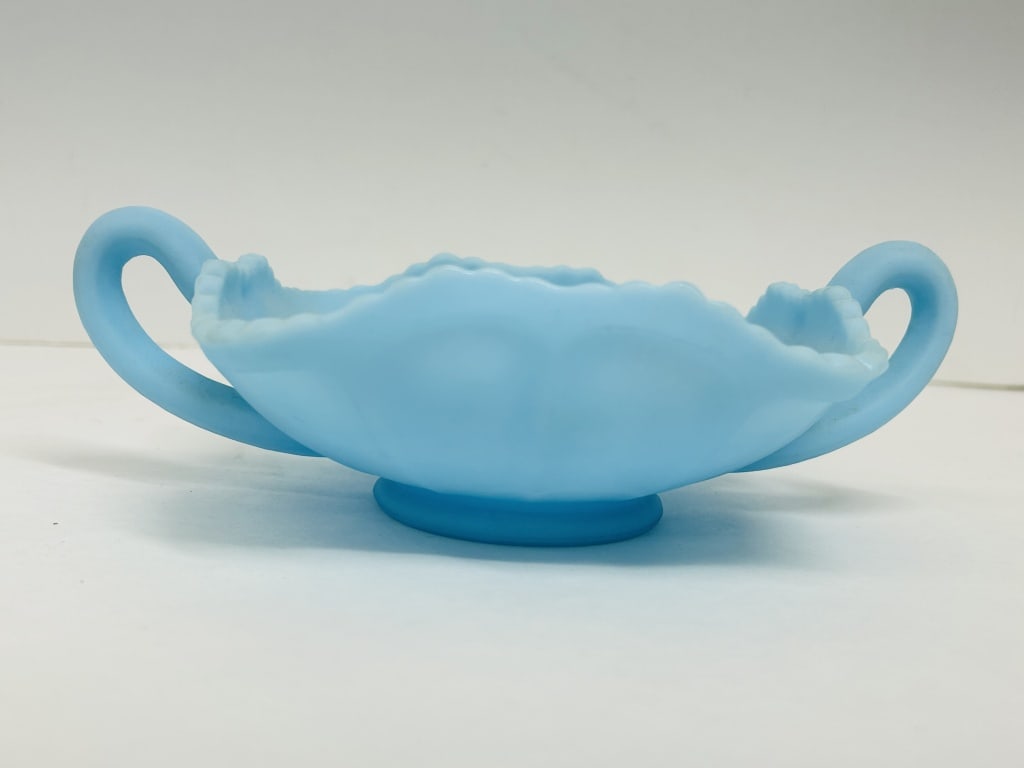FENTON BLUE SATIN GLASS DISH, 1970S: A light blue satin glass footed dish featuring twin handles, a ruffled rim, and a molded butterfly and floral interior motif. The Fenton script mark within an oval is present on the underside, signify